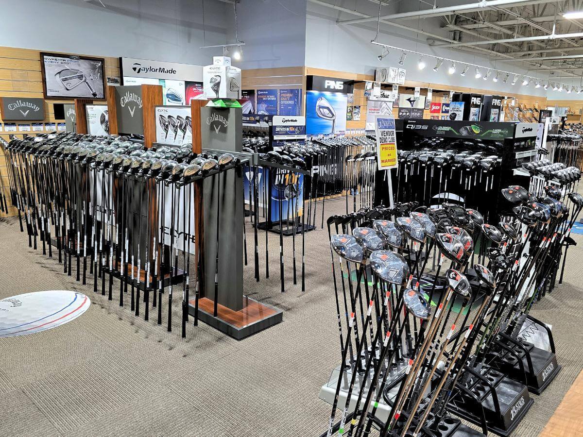 The interior of Austad's Golf Omaha Westwood where you can see racks of standing golf clubs on the store floor. Featuring name brands like Callaway and TaylorMade along with "on sale" used golf clubs.