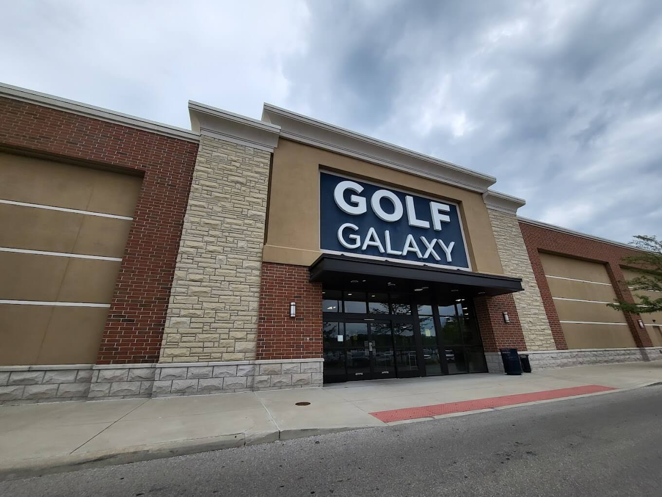 The exterior of Golf Galaxy in Columbus, Ohio during an overcast day in the summer. The building itself is beige and brick.