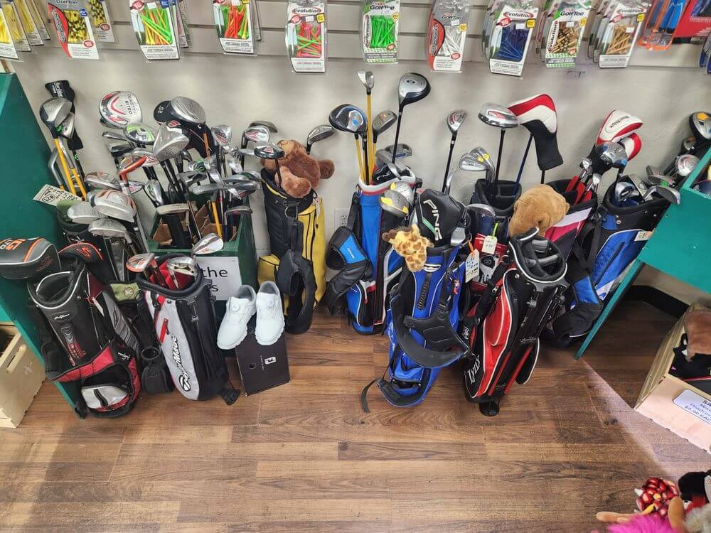 The store floor of Jerry's Golf Store where a variety of kids golf bags can be seen with used clubs sticking out of them. On the wall behind it are golf tees in  clear plastic boxes for sale