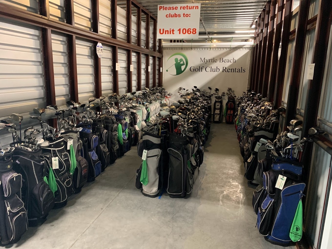 Neatly lined up rows of golf bags with gold clubs inside a storage unit.