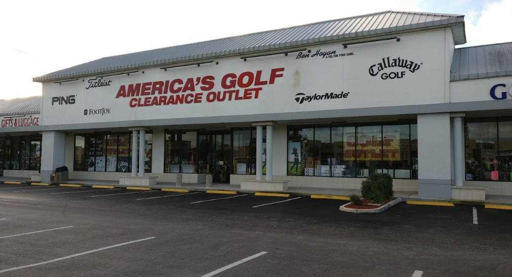 The outside of America's Golf Outlet Inc on a mostly cloudy summer day. The front of the building has golf brand names displayed all around the business name which is in big red lettering
