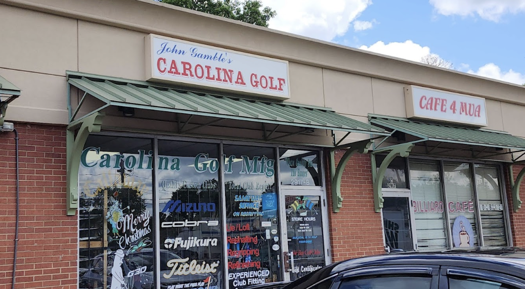 The exterior of Carolina Golf Manufacturing is a brick-faced storefront with lots of brand names on the windows and services offered. It is next to a Billiard Cafe.