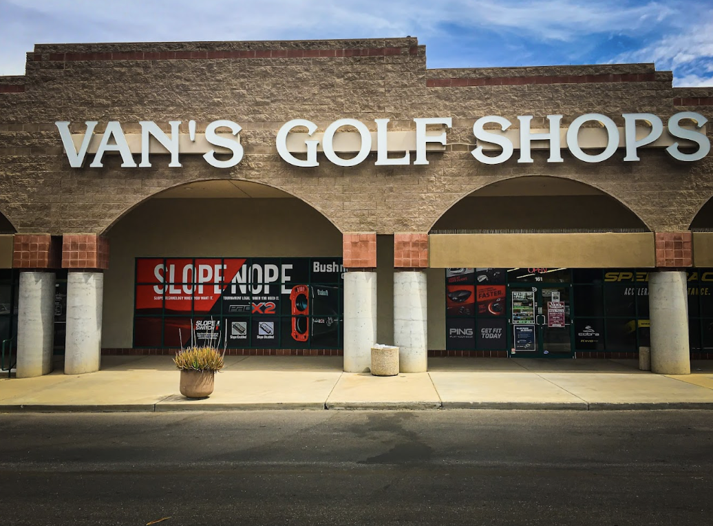 The exterior of Van's Golf Shop at the Crossroads Festival featuring a beige brick building and advertisements for clubs in the shop windows.