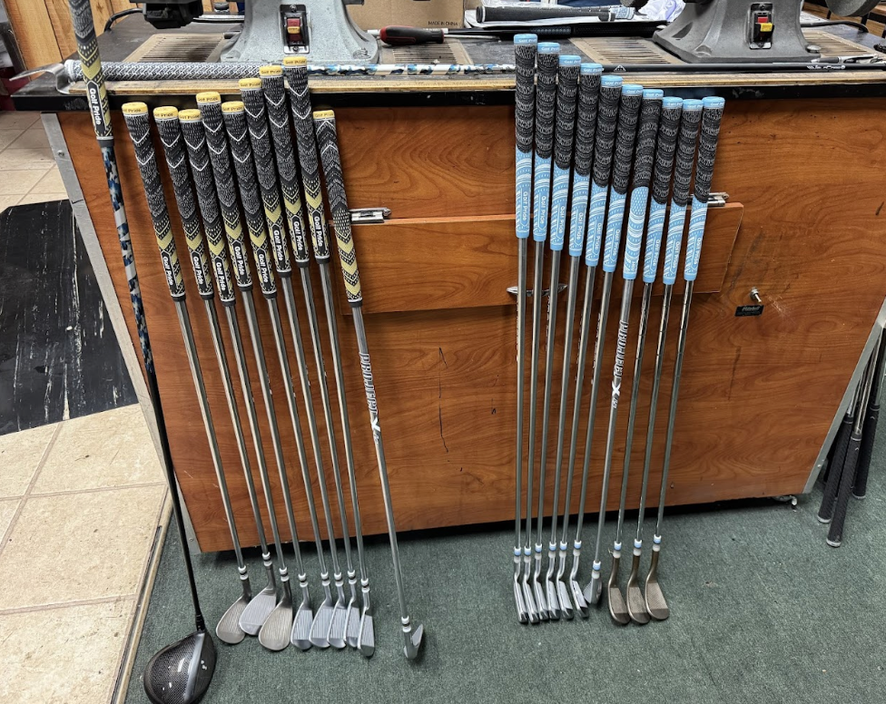 A close up of various used golf clubs leaning against a repair bench inside the store.