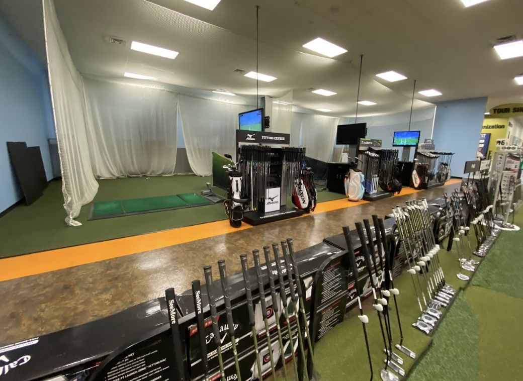 The inside of the Golf Galaxy showing off their hitting bays side-by-side with clubs waiting to be used leaning on boxes