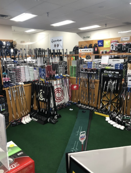 An inside look at the store featuring a putting green on the floor with a big supply of clubs leaning up against the sides of a smaller wall ready to be used.