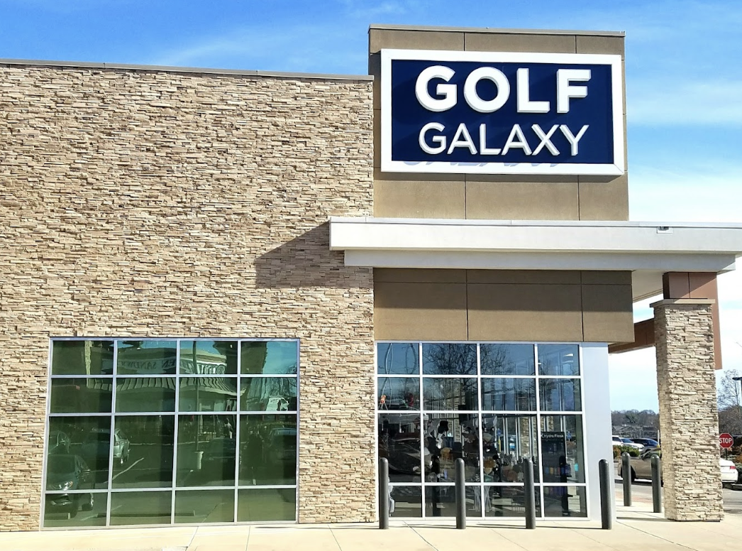 The exterior of Golf Galaxy is a tan rock building with big windows and a sign displaying the name of the store.